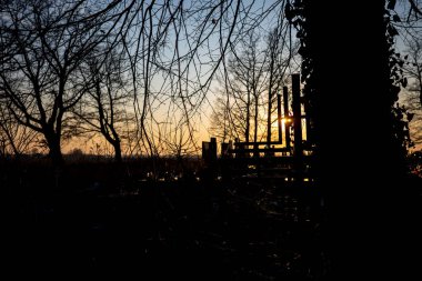 Silhouette of a cemetery cross against the orange sunset sky. Photo taken in autumn, just before evening.