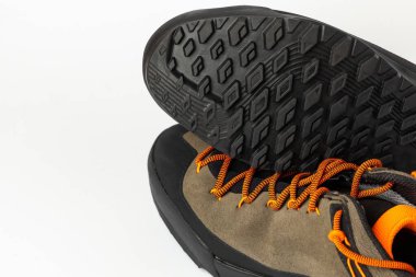 Beyaz arka planda renkli turuncu bağcıklı bej yürüyüş botları. Ayakkabının biri baş aşağı, tutucu tabanı gösteriyor. Fotoğraf yapay ışıklandırma altında çekildi.