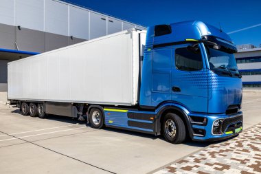 Lojistik merkezinin avlusuna park etmiş beyaz bir karavanı olan mavi bir kamyon. Kamyon yüklenmeyi ya da boşaltılmayı bekliyor. Fotoğraf güneşli bir günde çekildi..