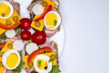 Yumurta, turşu, domates ve soğanlı tam buğday ekmeğinden yapılmış sağlıklı sandviçler beyaz tabakta servis edilir. Sandviçlerin olduğu tabak beyaz arka planda duruyor..