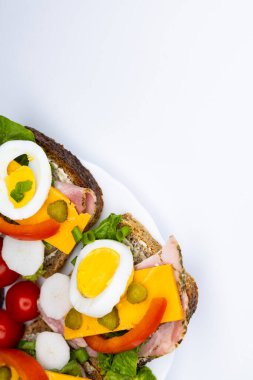 Yumurta, turşu, domates ve soğanlı tam buğday ekmeğinden yapılmış sağlıklı sandviçler beyaz tabakta servis edilir. Sandviçlerin olduğu tabak beyaz arka planda duruyor..