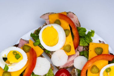 Yumurta, turşu, domates ve soğanlı tam buğday ekmeğinden yapılmış sağlıklı sandviçler beyaz tabakta servis edilir. Sandviçlerin olduğu tabak beyaz arka planda duruyor..