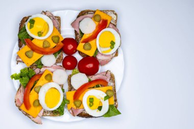 Yumurta, turşu, domates ve soğanlı tam buğday ekmeğinden yapılmış sağlıklı sandviçler beyaz tabakta servis edilir. Sandviçlerin olduğu tabak beyaz arka planda duruyor..