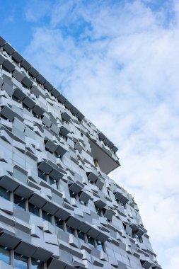 Modern bir konut ve ofis binasının gri cephesi. Bina duvarı açık bulutlu mavi bir gökyüzüne kurulmuş..