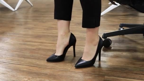 Vrouwelijke benen in zwart hoge hak schoenen in kantoor tikken hiel naar muziek — Stockvideo