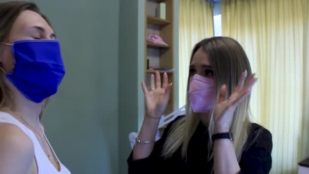 Kosmetikerin erklärt einer Frau den Eingriff. Beide in Masken — Stockvideo