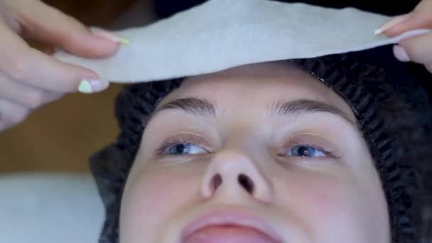 Jeune femme en bonnet jetable repose sur un lit, cosmétologue met serviette — Video