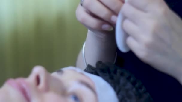 Kosmetolog sätter ögonlappar på kvinnan i engångshatt innan fransförlängning — Stockvideo