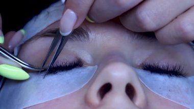 Kozmetik uzmanı, göz bandı takan kadınların takma kirpiklerini inceliyor.