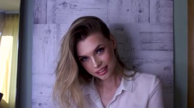 Doğal makyajlı güzel sarışın kadın kameraya bakıp gülümsüyor, saçlarını savuruyor.