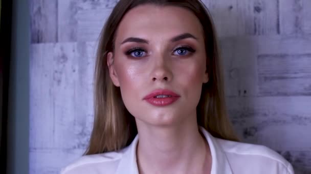 Jong blond vrouw met make-up kijkt in camera, draaien naar zijkanten — Stockvideo