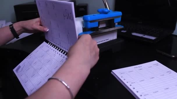 Женщина кладет бумагу с отверстиями на машину, чтобы сделать спиральный ноутбук — стоковое видео