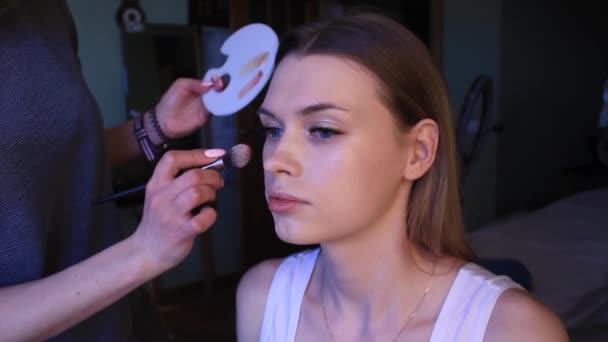 Jovem mulher branca loira recebe maquiagem profissional, MUA aplicando fundação — Vídeo de Stock
