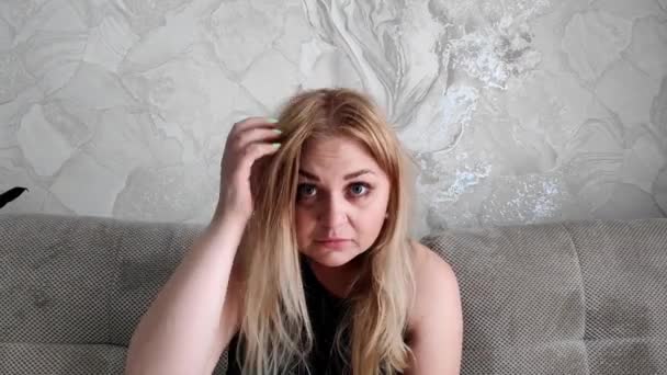 Blond wit vrouw kijkt in camera, scrathes haar hoofd, kijkt verward — Stockvideo