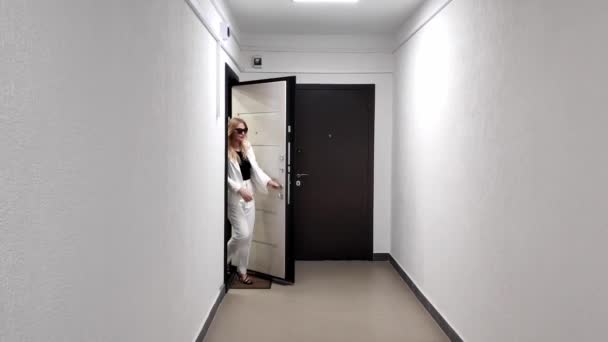 Белая женщина в белом костюме уверенно идет по белому коридору к камере — стоковое видео
