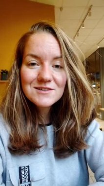 Bir kafede makyajsız neşeli genç bir kadın, dikey video çağrısı.