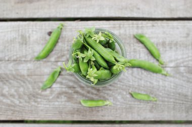 Mızraplı bezelye masanın üzerinde. Bir kavanoz içinde taze bezelye.