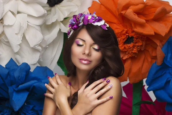 Retrato de beleza compõem-se de mulheres com uma coroa de flores em seu cabelo e grandes flores coloridas no fundo — Fotografia de Stock