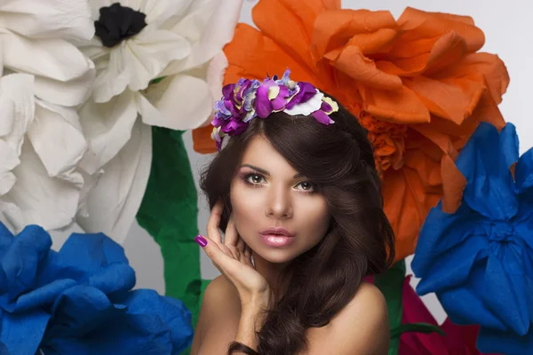 Retrato de beleza compõem-se de mulheres com uma coroa de flores em seu cabelo e grandes flores coloridas no fundo — Fotografia de Stock