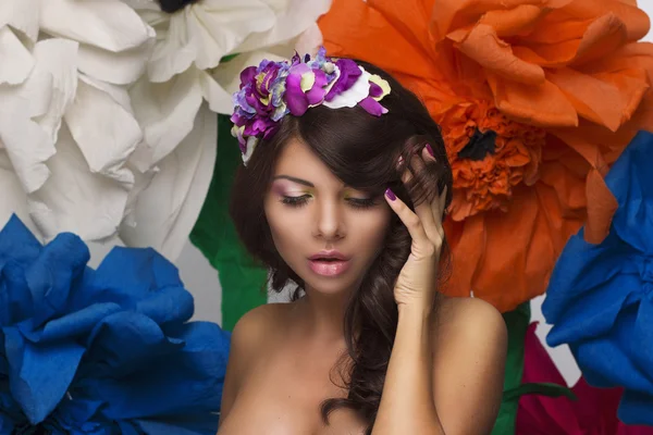 Retrato de beleza compõem-se de mulheres com uma coroa de flores em seu cabelo e grandes flores coloridas no fundo — Fotografia de Stock