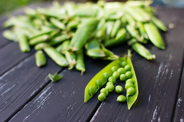 Frische grüne Erbsen auf dem schönen alten Holztisch verstreut — Stockfoto