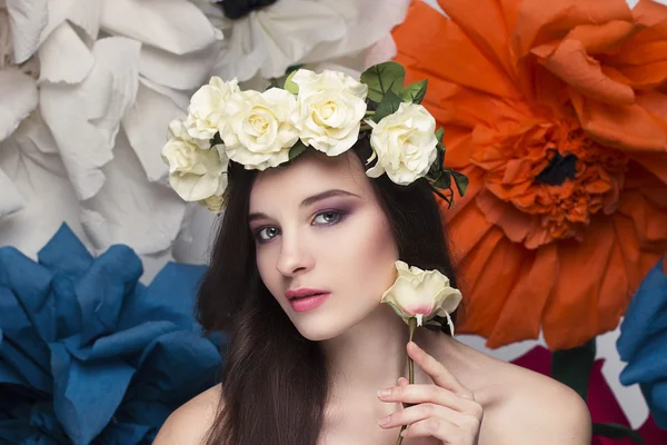 Ομορφιά πορτρέτο ενός μοντέλου με ένα στεφάνι από λουλούδια στο κεφάλι της, κρατώντας ένα μπουκέτο από τριαντάφυλλα και όμορφη μακιγιάζ — Φωτογραφία Αρχείου
