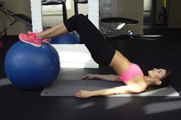 Hermosa chica instructor de fitness demuestra cómo hacer los ejercicios en un gimnasio con pelota de fitness — Foto de Stock