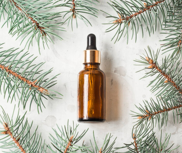 Плоская укладка бутылки янтарного масла для лица и пихты Tidewater Green веток косметических продуктов на белом фоне. Красивая квартира лежала с копировальным пространством. Изображение для салонов красоты и спа. Рождественская косметика