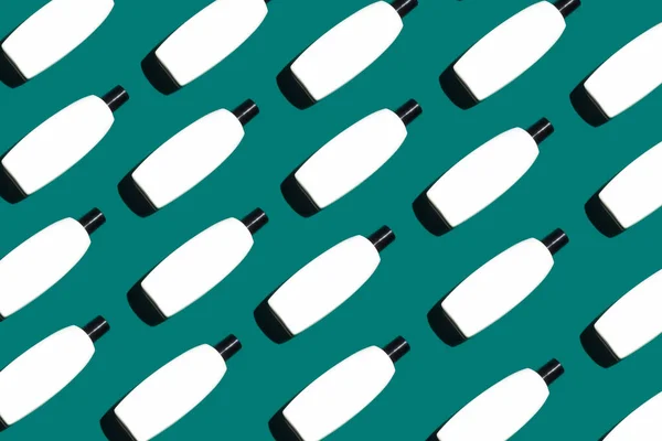 A pattern of the white blank cosmetic bottles on the pastel green background. Cosmetics flat lay. copy space