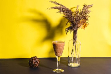 Sarı ve siyah arka planda kurutulmuş bir buket çiçekli, saplı bardakta içki. Kopyalama alanı olan arkaplan 2021 yılının trend rengi
