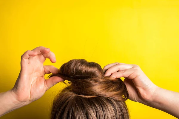 A woman makes a messy hair bun on her head. Yellow background. Copy space. Trend color of the year 2021