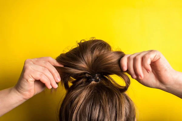 A woman makes a messy hair bun on her head. Yellow background. Copy space. Trend color of the year 2021