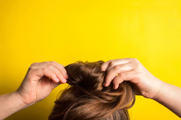 A woman makes a messy hair bun on her head. Yellow background. Copy space. Trend color of the year 2021