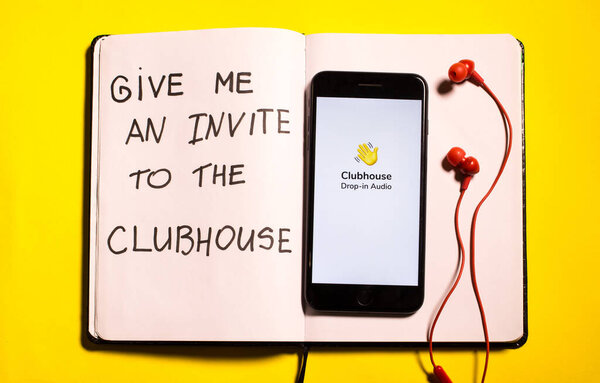 Riga, Latvia - February 24, 2021: Clubhouse drop-in audio application on the smartphone and earphones on the yellow background. New popular social media. Invite to the Clubhouse app
