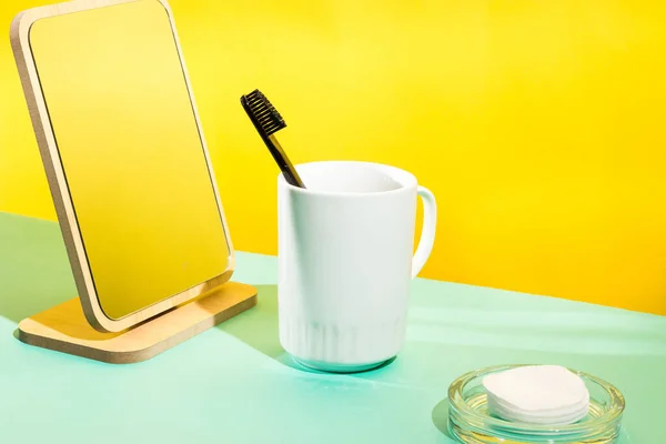 Black toothbrush in a glass in a modern colorful bathroom. Yellow background. Trend color of the year 2021