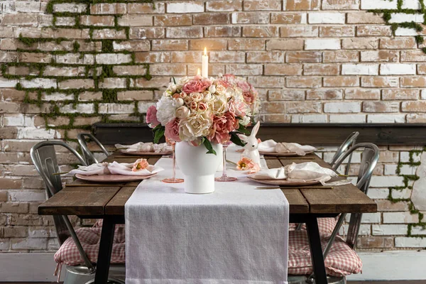 View of dreamy cute table decor with glasses flowers and lit candles. Wedding easter birthday holiday setup on a wooden table