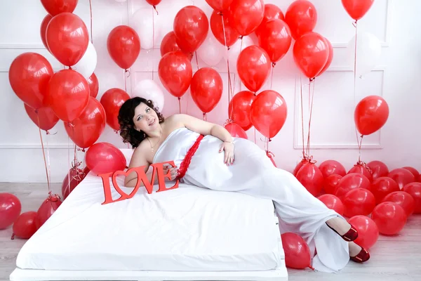 Genç hamile kadın aşk işaret ve kırmızı balonlar etrafında bir yatak üzerinde döşeme