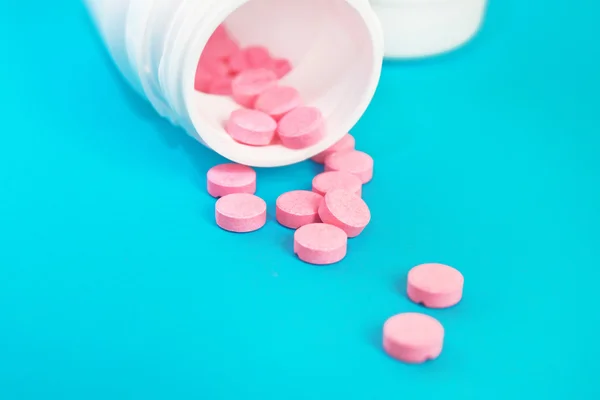 Pembe hap mavi zemin üzerine beyaz şişeden döktü