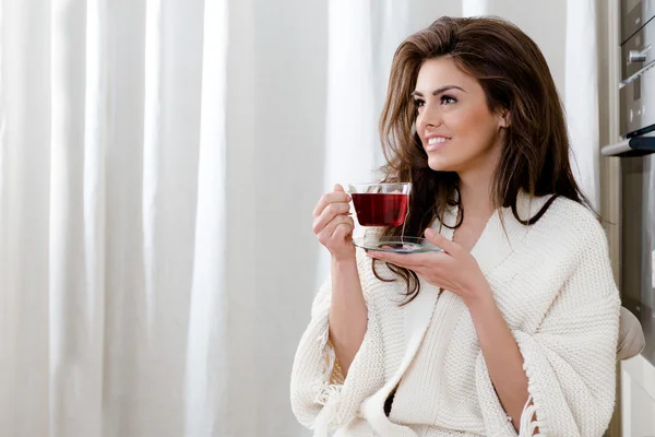 Mooie jonge vrouw drinken tea thuis in de keuken — Stockfoto