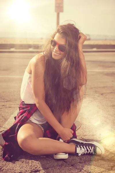 Schöne junge Frau, die über einem Skateboard sitzt. Hipster-Mädchen — Stockfoto