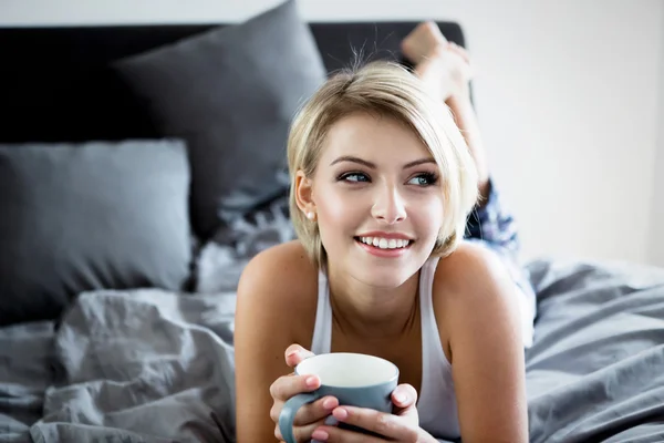 Donna sorridente che beve un caffè sdraiato a letto . — Foto Stock