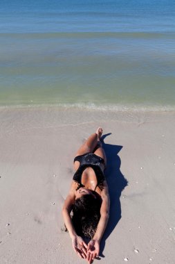 Kadın kumsalda yatıyor.