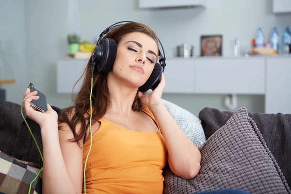Linda mujer sonriente tumbada en el sofá mientras escucha música — Foto de Stock