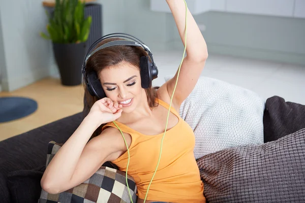 Linda mujer sonriente tumbada en el sofá mientras escucha música — Foto de Stock