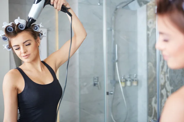Jonge vrouw krulspelden aanbrengend haar haar, badkamer — Stockfoto