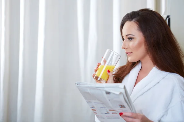 Frau liest Nachrichten, während sie Orangensaft trinkt — Stockfoto