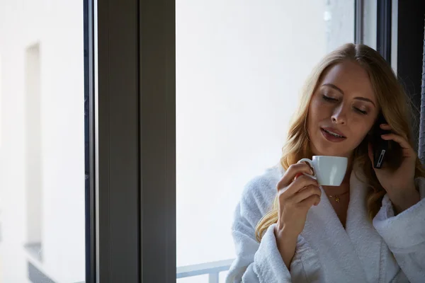 Молодая женщина разговаривает по телефону и пьет кофе — стоковое фото