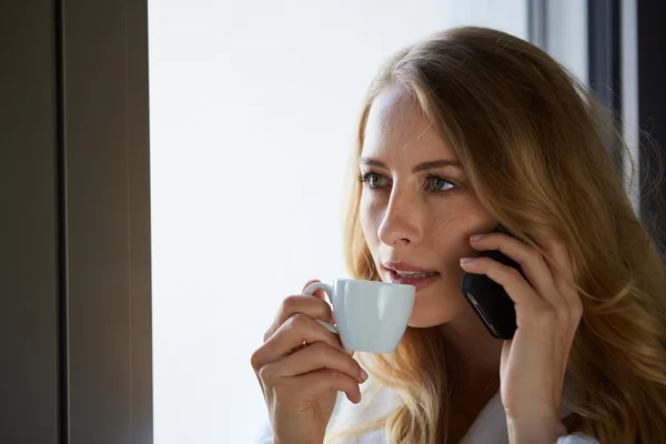 Young woman talking on the phone and drinking coffee — Stock Photo, Image