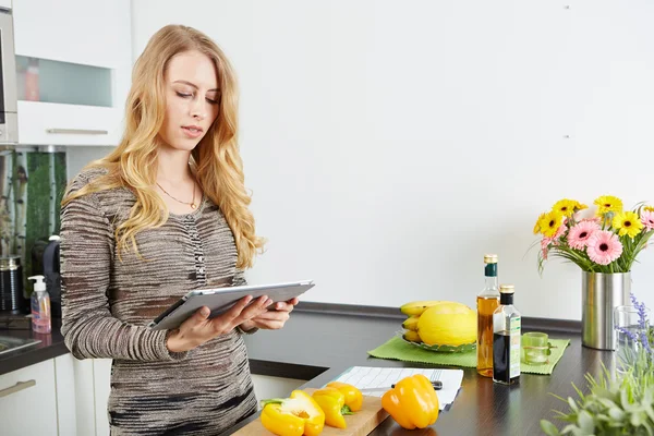 Mulher loira usando um computador tablet para cozinhar — Fotografia de Stock