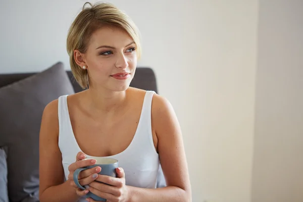 Glücklich lächelnde schöne blonde Frau, die mit einer Tasse Kaffee erwacht — Stockfoto